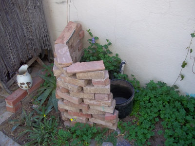 Greywater buckets behind stack of salvaged bricks